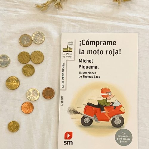 Foto en la que aparece el libro Cómprame la moto roja, junto a unas monedas